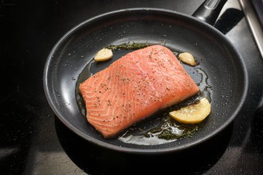 Taze somon fileto, limon, ot ve sarımsak ile kızartılır. Sobanın üstünde siyah bir tavada, kopyalama alanında, seçilmiş odak noktasında, dar bir alanda.