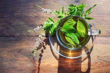 Taze nane yaprağından bitki çayı ve kırsal bir tahta masada cam bir fincanda çiçekler, yukarıdan yüksek açılı görüş, kopyalama alanı, seçilmiş odak, dar alan derinliği