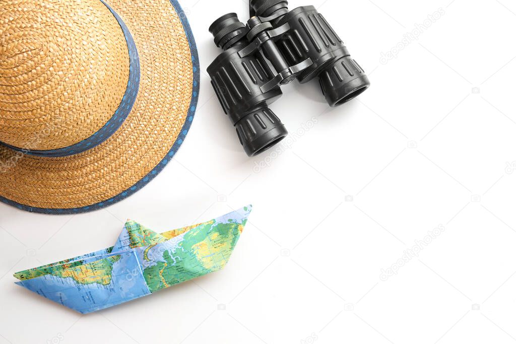 Straw hat, binoculars and a paper boat folded from a map on a white background, concept for cruise or vacation on the sea, copy space, selected focus