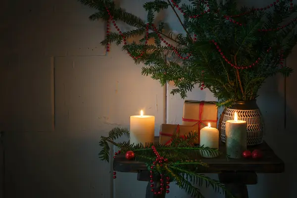 Christmas time with burning candles, gifts, evergreen branches and decoration on a small wooden table, cozy warm light in the dark season, copy space, selected focus, narrow depth of field