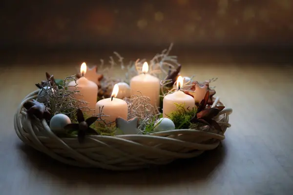 Advent wreath in natural tones made of wicker with beige candles, moss and Christmas decoration on a wooden table against a dark background, copy space, selected focus, narrow depth of field