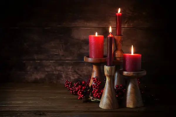Group of four red candles in candle sticks made of wood as advent decoration against a dark rustic wooden background, holiday home decor, copy space, selected focus, narrow depth of field