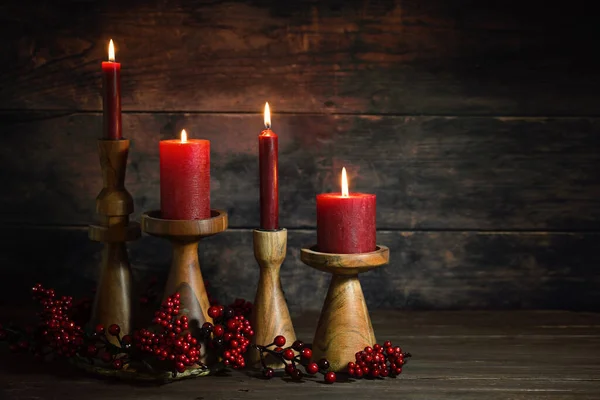 Four red candles in wooden candle sticks in a row as Advent or Christmas decoration against a dark rustic background, natural holiday home decor, copy space, selected focus, narrow depth of field