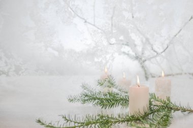 Dört yanan beyaz mum ve donmuş camın önünde bir köknar ağacı dalı ve karlı bir kış manzarası, ortaya ve Noel süslemesi, fotokopi alanı, seçilmiş odak, dar alan derinliği