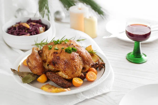Festive poultry dinner, roast chicken with fruits and herbs, served with red cabbage and wine on a white table pine branches, candles and Christmas decoration, holiday meal, copy space, selected focus