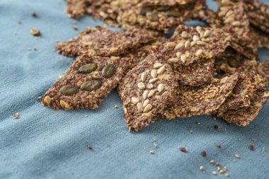 Yulaf ve keten tohumu ile pişirilmiş sağlıklı tuzlu, tam tahıllı hamur işi aperatifler, üzerinde çeşitli tohumlar, mavi peçete, kopya alanı, seçilmiş odak, dar alan derinliği