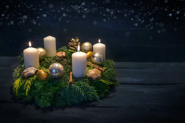 Green advent wreath with white candles, three are lit for third advent, Christmas decoration and cookies, dark blue wooden background with star bokeh, copy space, selected focus