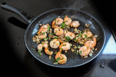 Kuyruklu karidesler, soğan, sarımsak ve otlarla kızartma tavasında kızartılır. Siyah bir sobanın tepesinde, deniz mahsulleri yemeği pişirilir. Kopya alanı, seçilmiş odak noktası, dar bir tarla derinliği.