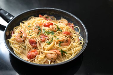 Karidesli, domatesli ve otlu spagetti fırının üstünde siyah bir tava, Akdeniz yemekleri yemeği pişirmek, fotokopi alanı, seçilmiş odak noktası, dar bir tarla derinliği.