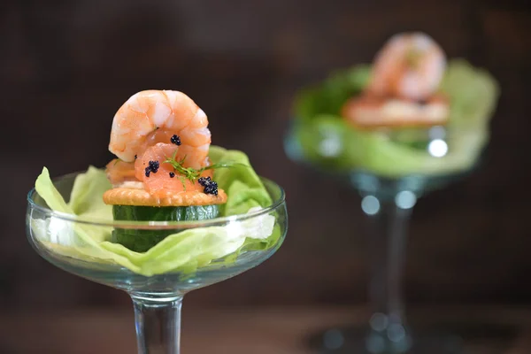 Appetizer or party snack with salmon, shrimp and caviar on lettuce served in a cocktail glass against a dark background for holidays like Christmas and New Year, copy space, selected focus