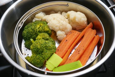 Karışık sebzeler, havuçlar, brokoli ve karnabahar bir gıda buhar sepetinde paslanmaz çelik bir tencerede, mineralleri, vitaminleri ve tatları koruyan sağlıklı pişirme metodu, seçilmiş odak, dar alan derinliği
