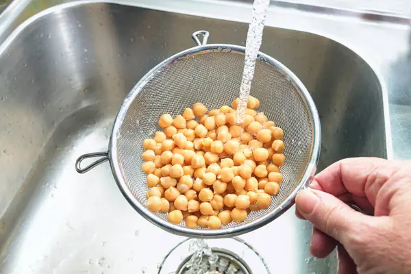 Pre-cooked canned chickpeas are rinsed with water in a sieve over the sink before being used in various dishes, healthy legumes are rich in protein, fiber and minerals, copy space, selected focus
