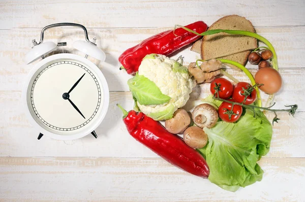 Interval fasting or IF, food products, and an alarm clock indicate the period of time during which it is allowed to eat, diet concept for losing weight, flat lay, top view from above, selected focus