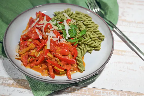 Healthy vegan meal from green legume-based noodles with red vegetable ragout from bell pepper and tomato, high in protein, vitamins, dietary fibers and minerals, copy space, selected focus