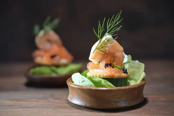 Party snack from shrimp, salmon, caviar and dill garnish in small wooden bowls on a dark rustic table, appetizer for holidays like Christmas, Thanksgiving or New Year, copy space, selected focus