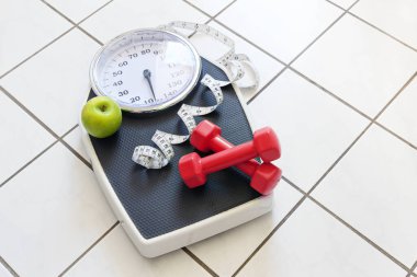Kırmızı halterli kişisel ölçek, mezura ve fayanslı zeminde yeşil elma, spor ve kilo kaybı konsepti, kopyalama alanı, seçili odak noktası