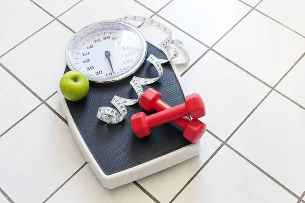 Kırmızı halterli kişisel ölçek, mezura ve fayanslı zeminde yeşil elma, spor ve kilo kaybı konsepti, kopyalama alanı, seçili odak noktası