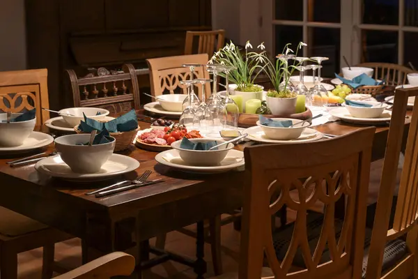 有各种旧椅子的大型木制桌子 装有白色陶器的节日套件 酒杯和装饰品 供家人和朋友晚上在餐厅里随意举行的晚宴用 图库图片