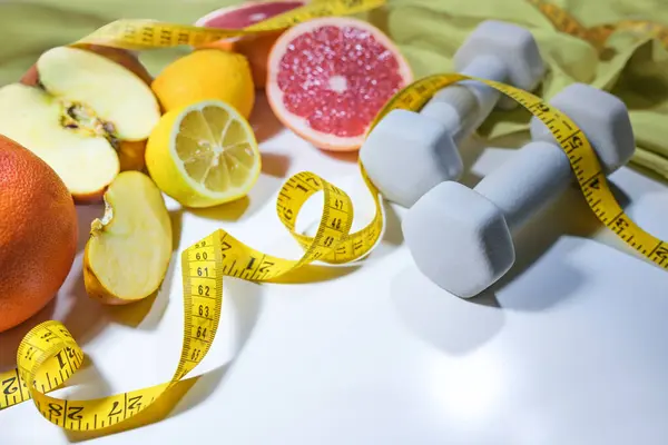 新鲜柑橘类水果 测量带子和哑铃 健康的生活方式概念与健康 运动和维生素丰富的食物 浅灰背景 复制空间 选定焦点 图库图片