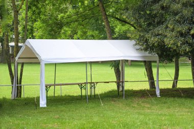 Parktaki bir çayırda ağaçların altına kurulmuş boş beyaz parti çadırı. Yaz festivali için hazırlık. Kopya alanı, seçilmiş odak noktası.