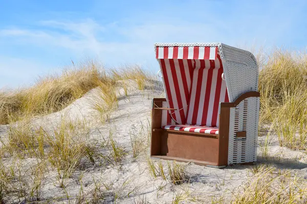 Red and white striped wicker beach chair in the dunes between dry marram grass at the Baltic Sea against a blue sky, happy summer vacation greeting card, copy space, selected focus