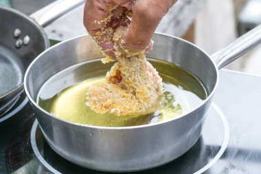 Bir parça ekmekli tavuğu kaynamış yağlı tencereye dikkatlice koy. Kızartma, pişirme konsepti, seçilmiş odak ve dar alan derinliği için.