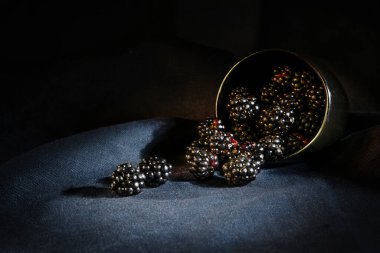 Taze toplanmış yabani böğürtlenler siyah bir kaseden koyu bir peçeteye yuvarlanıyor, karamsar, yaz meyvelerinin durgun yaşamı, fotokopi alanı, seçilmiş odak, dar alan derinliği