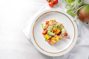 Karides, karides, mango, avokado, marul ve domatesli deniz ürünleri salatası. Zarif beyaz tabakta sebze sosu, aperatif menü, yukarıdan yüksek açılı manzara, kopyalama alanı, seçilmiş odak noktası.
