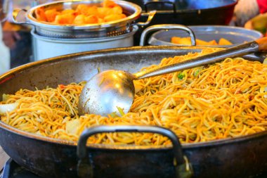 Büyük bir kepçeyle Çin usulü kızarmış erişte, açık hava festivalinde sokak yemeği, seçilmiş odak, dar alan derinliği.