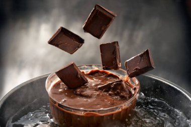 Çikolata parçaları, eriyen su banyosunda cam bir kaseye düşüyor. Kopyalama alanı, seçilmiş odak, dar alan derinliği.