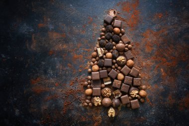 Çikolata ve pralinler karanlık bir arkaplanda Noel ağacı şeklinde serilmiş, mevsimlik tatil tatlıları, yukarıdan en iyi manzara, büyük kopya alanı, seçilmiş odak noktası. 