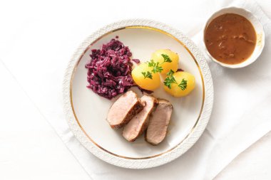 Domuz eti dilimleri, kırmızı lahana ve patates maydanozlu garnitür beyaz tabakta ve et sosu hafif bir masada, yukarıdan yüksek açılı görüş, kopyalama alanı, seçilmiş odaklanma alanı