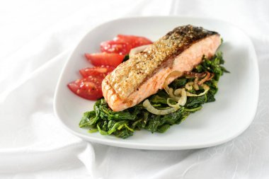 Ispanak sebzeli, soğanlı ve domatesli kızarmış somon filetosu, beyaz tabak ve masa örtüsünde düşük karbonhidratlı diyet için sağlıklı yemek, kopyalama alanı, seçilmiş odak noktası.