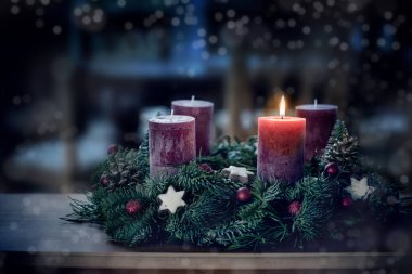 İlk yanan mum ve Noel süslemesi ile advent çelenk gece mavi ışık, karlı bokeh, fotokopi alanı, renkli fotoğraf, seçilmiş odak, dar alan derinliği