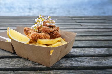 Limon dilimli balık ve patates kızartması ve eskimiş ahşap bir rıhtımda karton bir kutuda lahana filizleri.