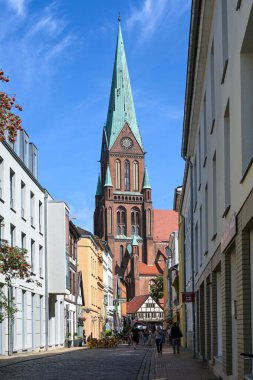 Schwerin, Almanya, 29 Temmuz 2024: Dar yol Buschstrasse 'de küçük dükkanlar ve sokak restoranları tarihi eski şehir, ünlü turizm merkezi St. Marien katedraline çıkıyor.