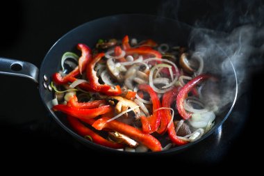 Canlı kırmızı biber dilimleri, mantarlı ve soğanlı sıcak buharda kızartılmış tavada siyah indüksiyon hob, karıştırılmış sebzeler, kopyalama alanı, seçilmiş odak, dar alan derinliği.