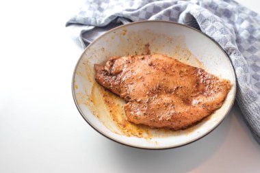 Tavuk göğsü fileto yağı ve tuz, biber ve kırmızı biber gibi baharatlarla marine edilmiş, kızartma ya da kızartma için hazırlık, arka planda gri tabak ve mutfak havlusu, kopyalama alanı, seçilmiş odak noktası