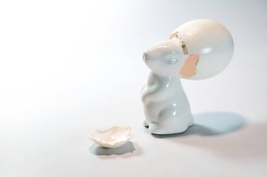 Beyaz seramik Paskalya tavşanı kafasında şapka gibi boş bir yumurta kabuğu, komik mevsimlik tebrik kartı, ışık arkaplanı, fotokopi alanı, seçilmiş odak, dar alan derinliği