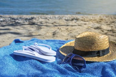 Hasır şapka, parmak arası terlik ve güneş gözlüğü. Baltık Denizi 'nin doğal bir sahilinde güneşli bir günde. Yaz tatili konsepti.