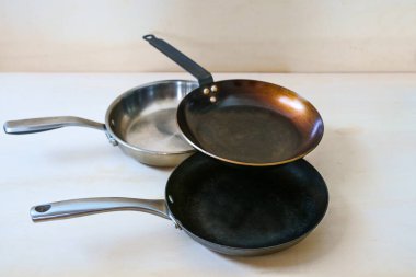 Karbon çeliğinden, paslanmaz çelikten yapılmış sağlıksız yapışmamış üç tava ve hafif ahşap zemin üzerine dökme demir, kopyalama alanı, seçilmiş odak, dar alan derinliği