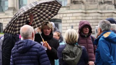 BERLİN, GERMANY - CIRKA MAYIS 2019: Şemsiyeli kadın ve bir binanın önünde duran diğer insanlarla konuşuyor (4K, 30fps)