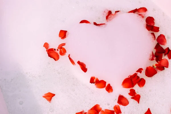 St. Valentine\'s Day bath. Aromatherapy with flower petals. Take a bath. Water with white foam. Roses float in the bathroom.