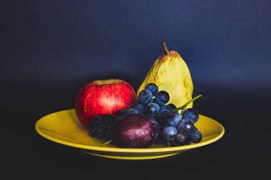 Still life with fruits on a dark blue background. Grapes, cream, pear and apple