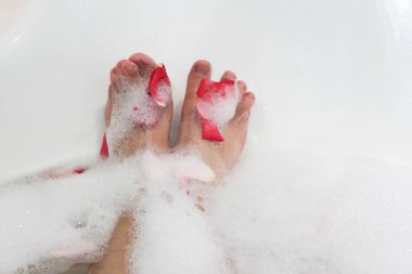 Relax. Romantic. Red rose petals in bath with legs girl. Valentine's Day