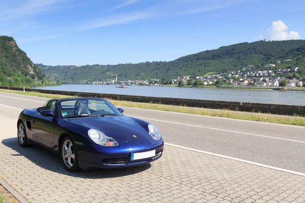 Boppard, Almanya - 26 Haziran 2021: Mavi Roadster Porsche Boxster 986 ve Rhine Vadisi Panoraması. Araba, Alman otomobil şirketi Porsche tarafından üretilen iki koltuklu bir spor arabadır..