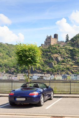 St. Goar, Almanya - 26 Haziran 2021: Mavi Roadster Porsche Boxster 986 ile Rhine Vadisi ve Katz Kalesi Panoraması. Araba, Alman otomobil şirketi Porsche tarafından üretilen iki koltuklu bir spor arabadır..