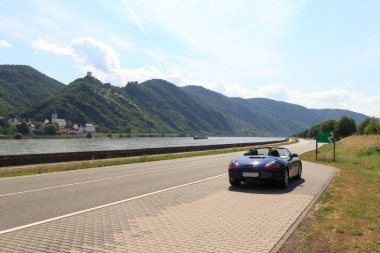 Boppard, Almanya - 26 Haziran 2021: Mavi Roadster Porsche Boxster 986 Rhine geçidi ve kale panoraması. Araba, Alman otomobil şirketi Porsche tarafından üretilen iki koltuklu bir spor arabadır..