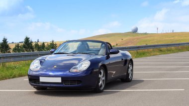 Gersfeld, Almanya - 23 Temmuz 2021: Mavi Roadster Porsche Boxster 986, Wasserkuppe Panorama ve Radar Kubbesi Rhoen Dağları 'nda. Araba, Porsche tarafından üretilen iki koltuklu orta-motorlu bir spor araba..