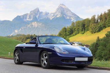 Berchtesgaden, Almanya - 25 Temmuz 2021: Mavi Roadster Porsche Boxster 986, Watzmann dağı ve sis panoraması. Araba, Porsche tarafından üretilen iki koltuklu orta-motorlu bir spor araba..